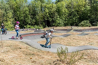 Kinder mit Rollern und Rädern auf Pumptrack