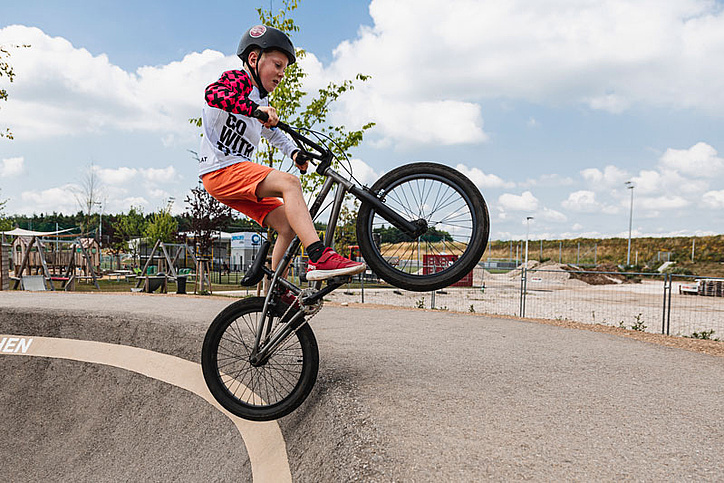 Junge auf Fahrrad macht einen Trick über die Kante vom Pumptrack