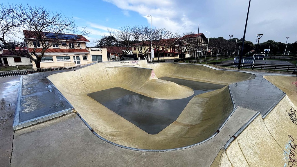 Vue panoramique du skatepark en béton vide à Biscarrosse sous un ciel nuageux.