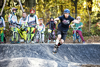 Inline skater in curve from pumptrack with spectators in background