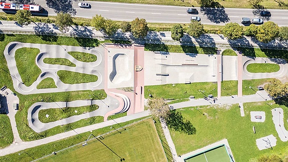 Aerial view of the Urban Sports Park Füssen with pump track, bowl, street and play area, adjacent to sports facilities.