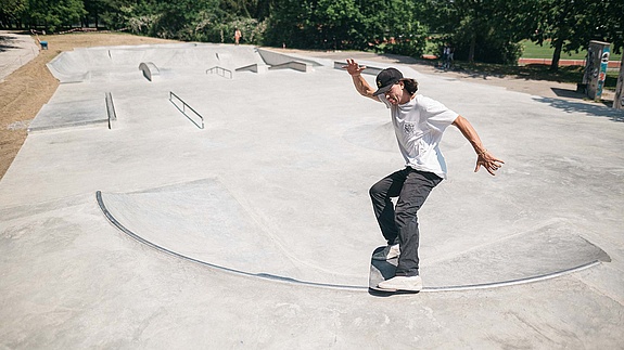 Skate boarder with white T-shirt does a trick in a concrete in-situ skate park