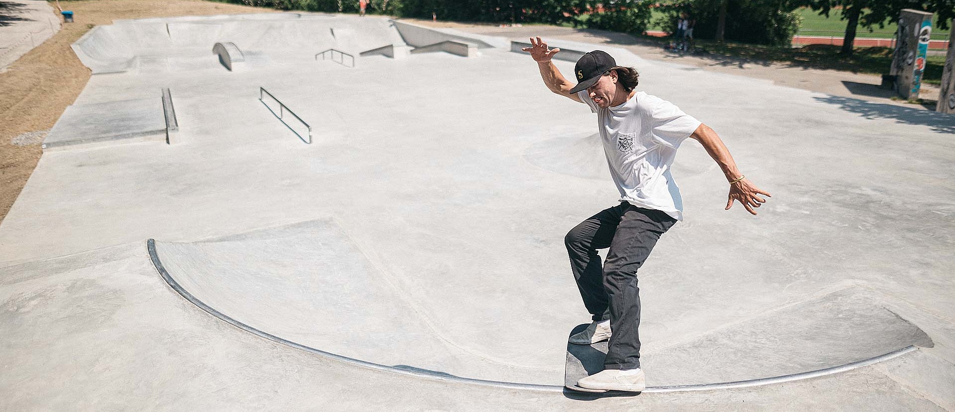 Skate boarder with white T-shirt does a trick in a concrete in-situ skate park