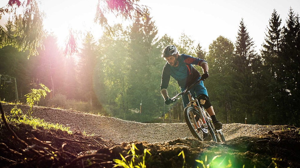 Mountainbiker in einer Kurve auf einem Flowtrail am Waldrand