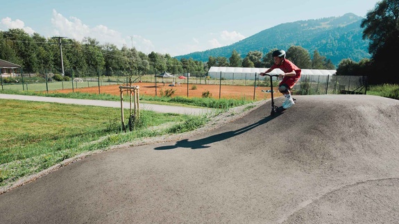 Scooter rider on pump track with mountain view