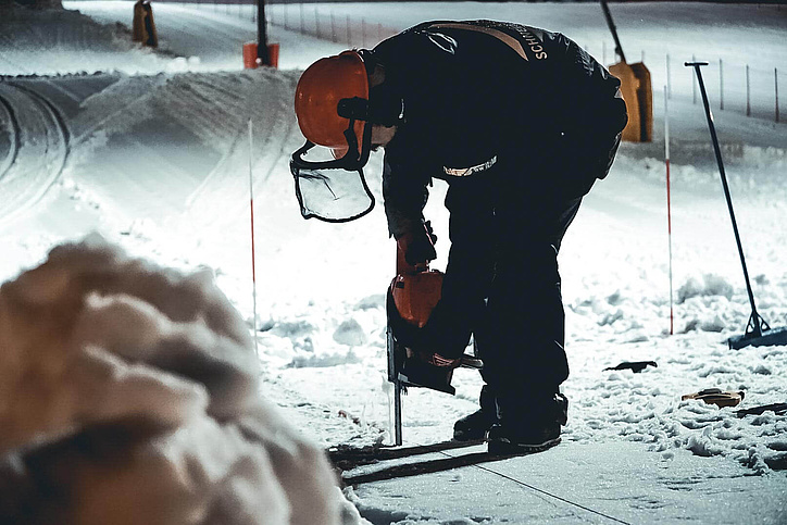 Arbeiter mit Sicherheitsbekleidung bohrt in den Schnee