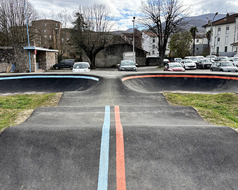 Vue de face d'une piste de pumptrack en asphalte à Saint-Girons avec des marquages au sol bleus et rouges.