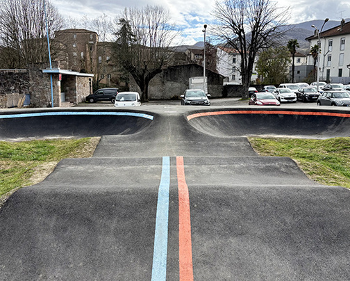 Vue de face d'une piste de pumptrack en asphalte à Saint-Girons avec des marquages au sol bleus et rouges.