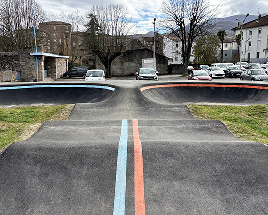 Vue de face d'une piste de pumptrack en asphalte à Saint-Girons avec des marquages au sol bleus et rouges.