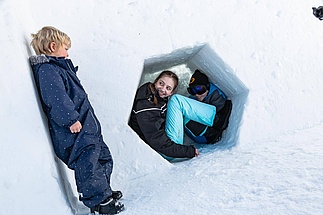 [Translate to Französisch:] Mädchen versteckt sich in einem Schneeloch vor kleinem Jungen