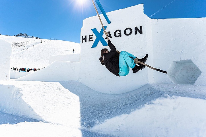 [Translate to Französisch:] Mädchen schwingt an Seil vor Hexagon Logo