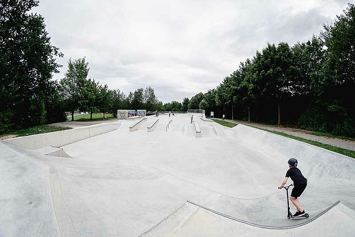 Kind mit Scooter fährt in leerem Ortbeton Skatepark