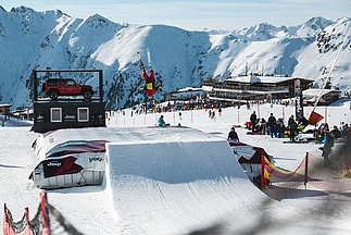 Skifahrer springt im Snowpark mit Gasthaus im Hintergrund
