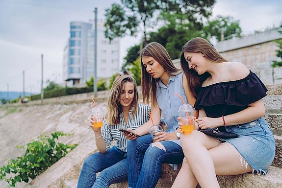 Three girls sitting with drinks on stone stairs in urban environment