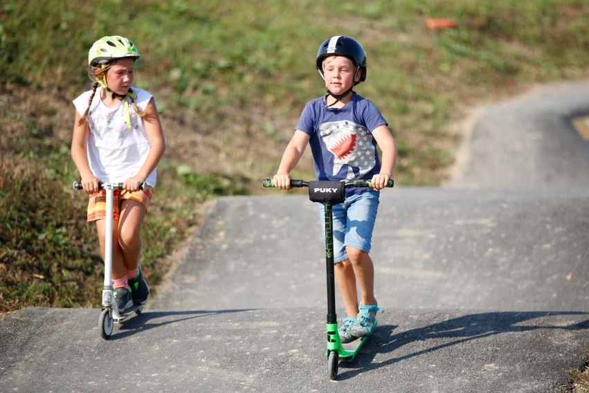 Two children with scooters on asphalt track