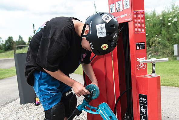 Boy repairs his scooter at a red service station at Urban Sports Park Durach.