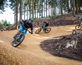 Zwei Biker fahren eine Kurve auf einem neu gebauten Bikepark im Wald
