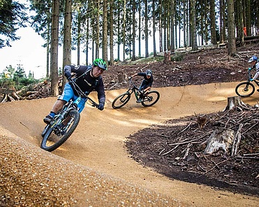 Zwei Biker fahren eine Kurve auf einem neu gebauten Bikepark im Wald