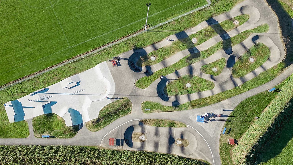 Drohnenaufnahme des gesamten Parks mit Skatepark und Pumptrack in direkter Nachbarschaft zu einem Fußballfeld.