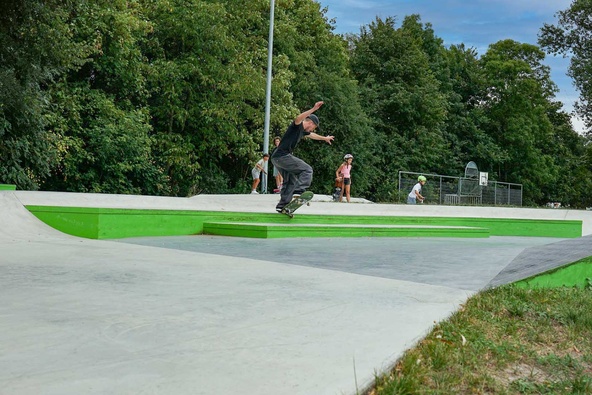 Close-up of a skateboarder performing a trick on a green concrete curb at Stockerau skatepark.