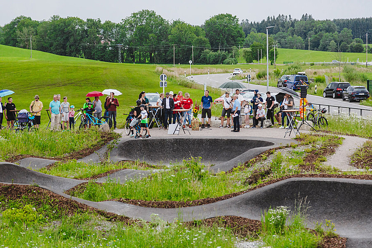 Many people at the opening of the pumptrack with green meadow in the background