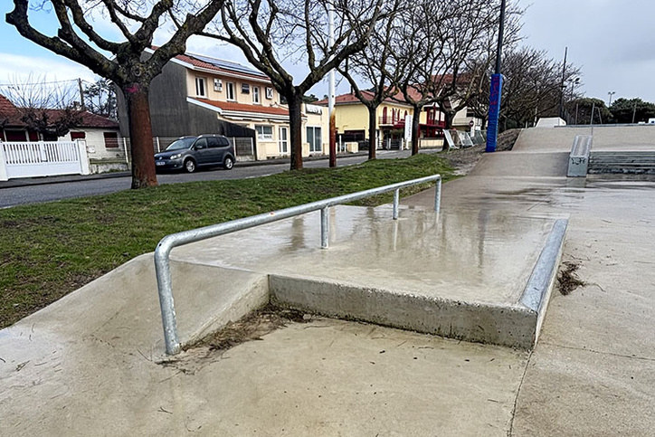 Metall-Rail auf einer Betonrampe im Skatepark Biscarrosse bei nassem Wetter und kahlen Bäumen.