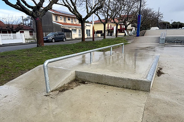 Metall-Rail auf einer Betonrampe im Skatepark Biscarrosse bei nassem Wetter und kahlen Bäumen.