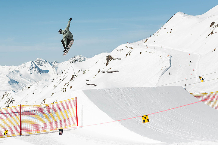 Snowboarder jumps over jump in snow park Ischgl