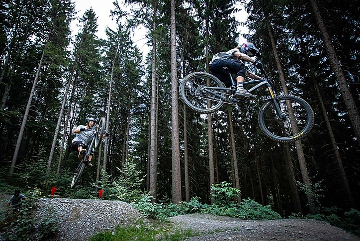 Two bikers jump on jump line in forest