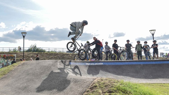 BMX rider jumps over the pump track at Urban Sports Park Hückelhoven, spectators watch the event.