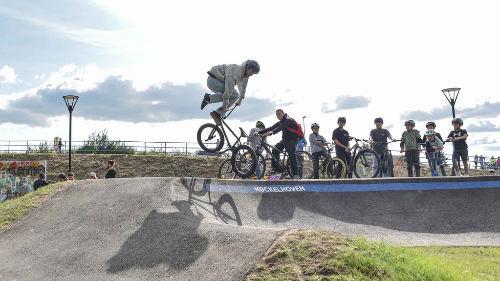 BMX rider jumps over the pump track at Urban Sports Park Hückelhoven, spectators watch the event.