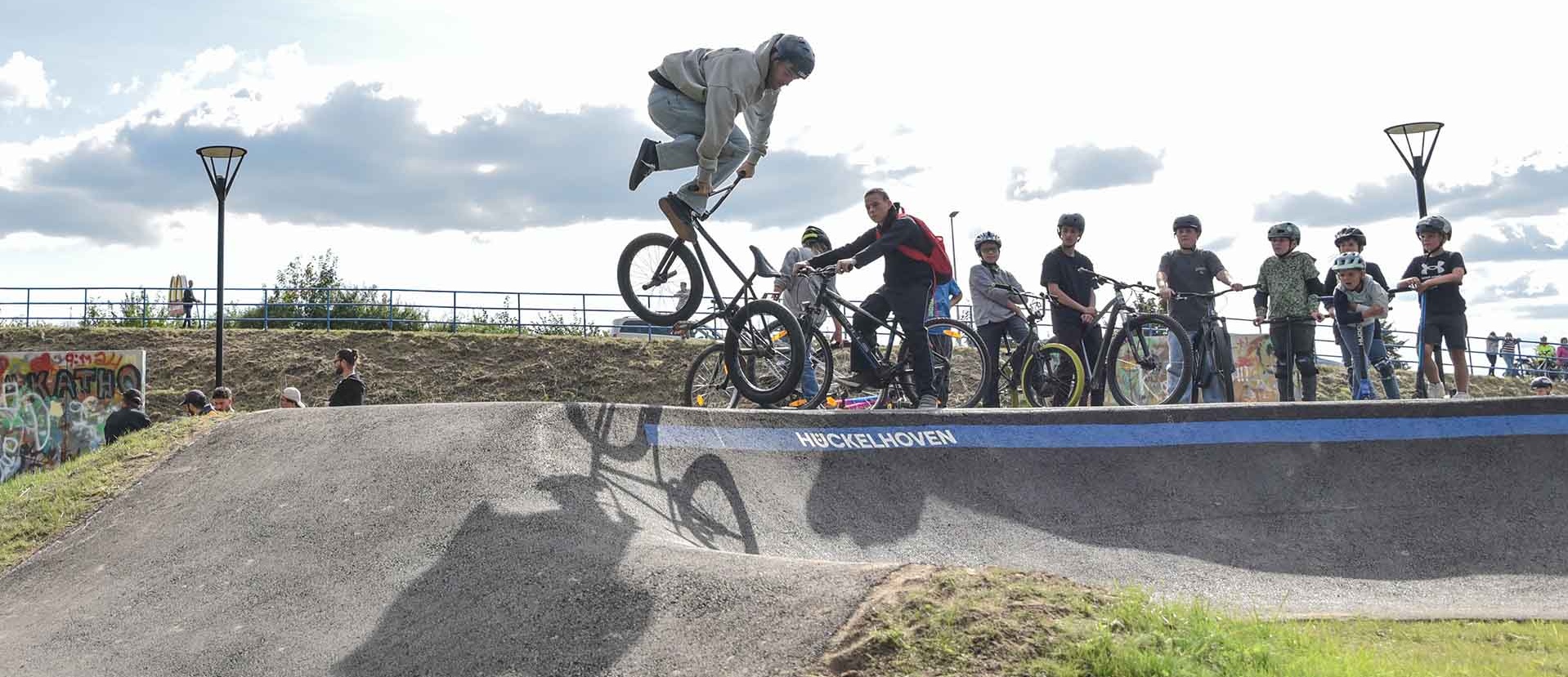 BMX rider jumps over the pump track at Urban Sports Park Hückelhoven, spectators watch the event.