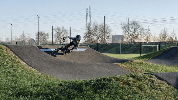 Mountainbiker fährt sportlich in einer markierten Steilkurve auf einer asphaltierten Pumptrack-Anlage.