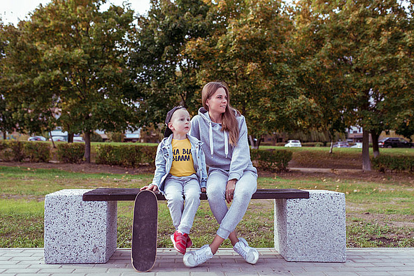 Mother sitting with child and skateboard on park bench