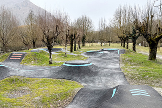 Bodenperspektive der Asphalt-Wellen und Kurven des Pumptracks in Saint-Béat-Lez mit roten Richtungspfeilen.