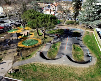 Luftaufnahme des Pumptracks und des angrenzenden Spielplatzes in Saint-Girons mit einem Radfahrer auf der Strecke.