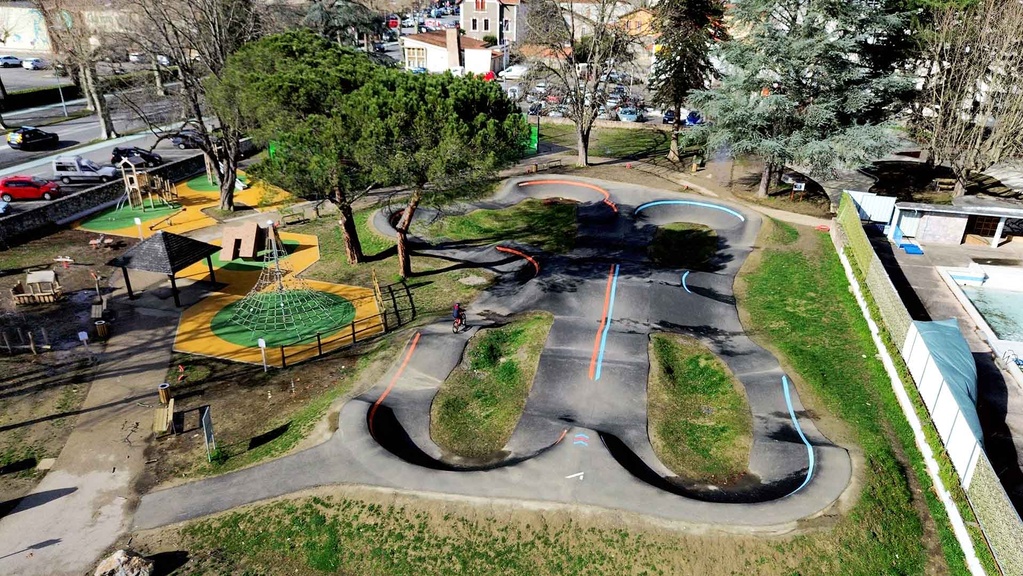Luftaufnahme des Pumptracks und des angrenzenden Spielplatzes in Saint-Girons mit einem Radfahrer auf der Strecke.