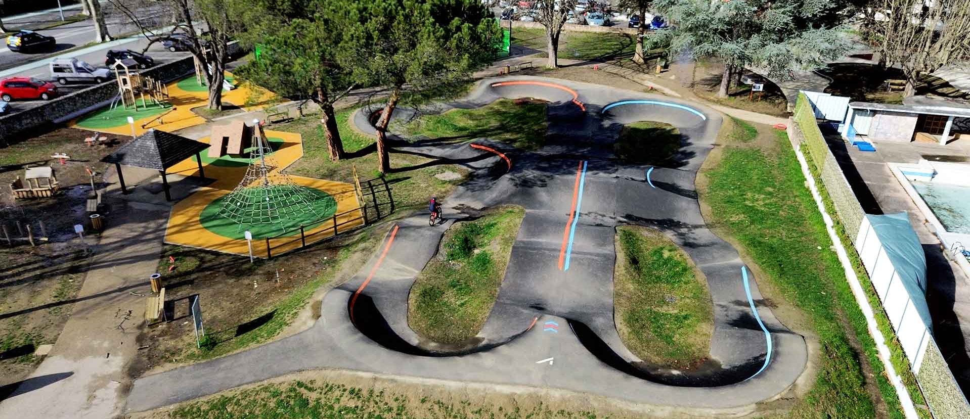 Luftaufnahme des Pumptracks und des angrenzenden Spielplatzes in Saint-Girons mit einem Radfahrer auf der Strecke.