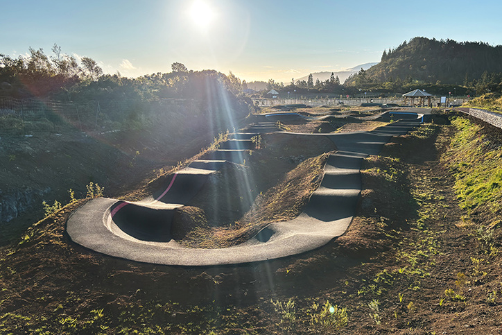 Asphalt pump track with rollers and berms under a bright sun in Le Tampon.