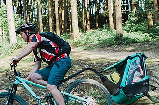 Mountain biker with child trailer riding down a trail