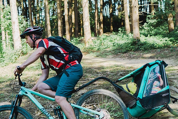 Mountain biker with child trailer riding down a trail