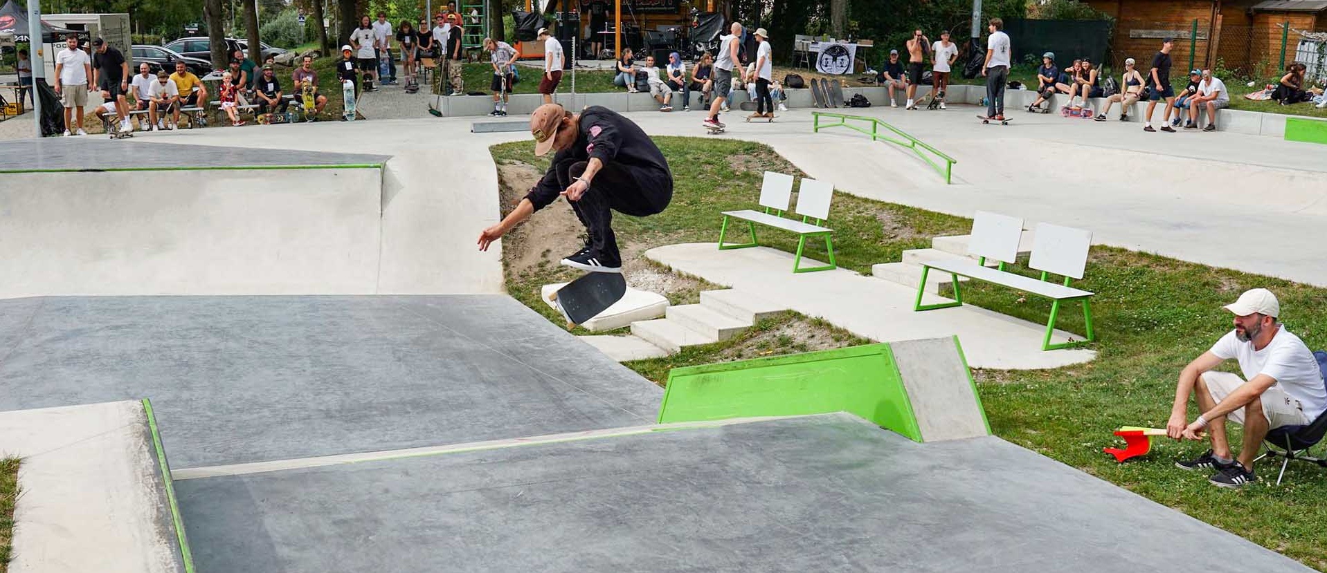 Skateboarder performing a kickflip over a ramp at Stockerau skatepark during a public event.