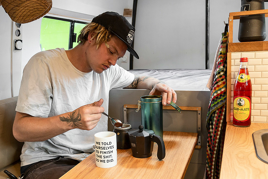 Boy sits in his van an prepares a coffee