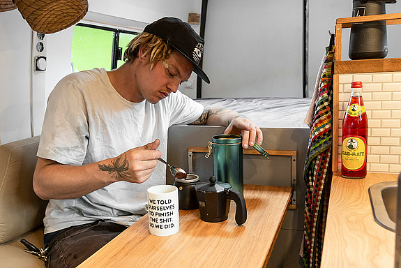 Boy sits in his van an prepares a coffee