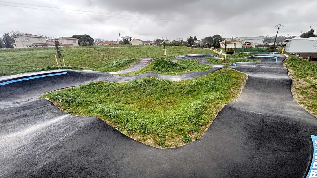 Aperçu grand angle du spacieux pumptrack de Saint-Geniès-Bellevue sous un ciel nuageux.