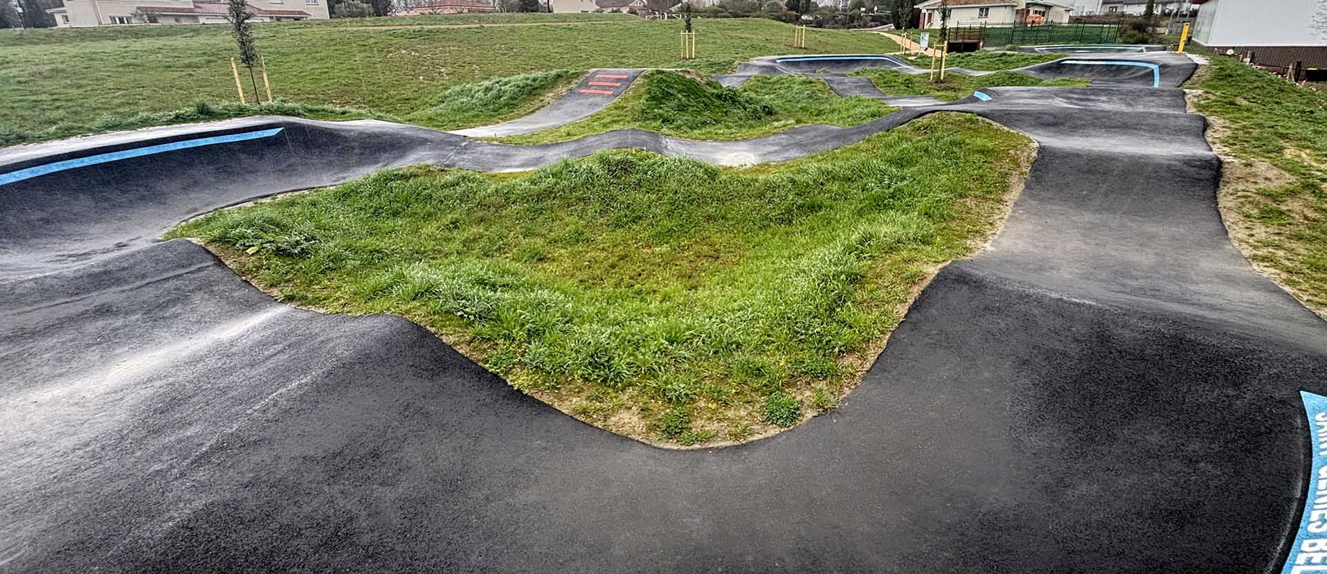 Aperçu grand angle du spacieux pumptrack de Saint-Geniès-Bellevue sous un ciel nuageux.