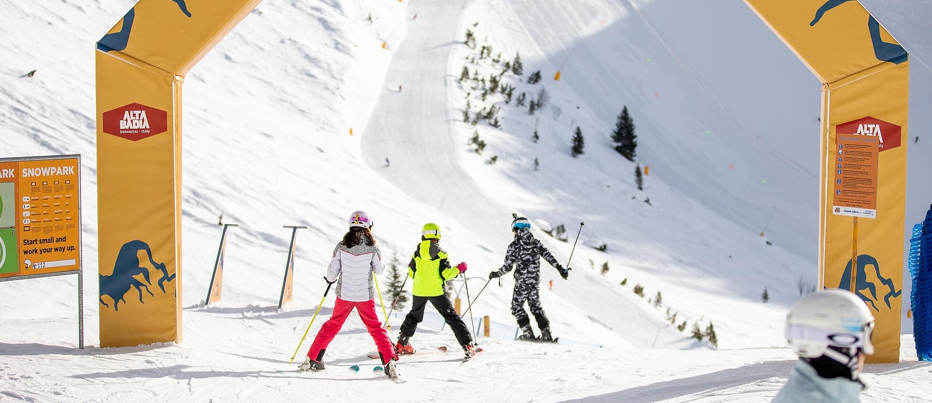 Drei Skifahrer fahren auf Piste durch Torbogen