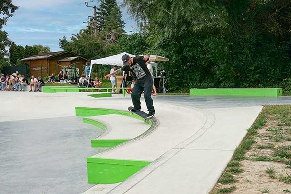 Skater vollführt einen Grind an einer geschwungenen Betonmauer mit grüner Kante in Stockerau.