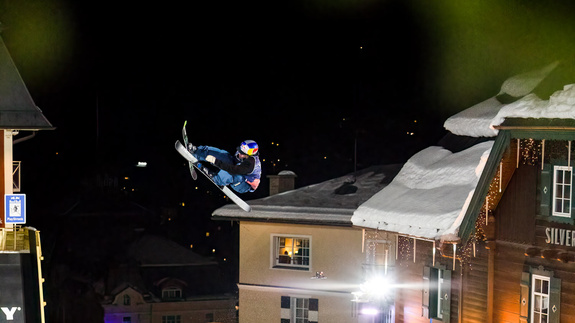Skifahrer macht Trick in der Luft vor Häusern und dem Nachthimmel
