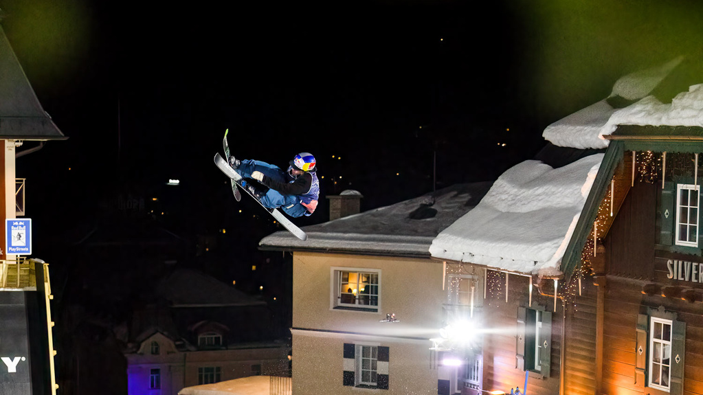 Skifahrer macht Trick in der Luft vor Häusern und dem Nachthimmel